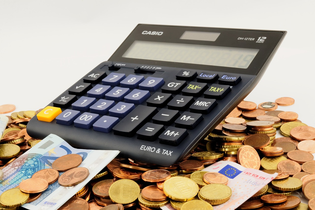 In dem Bild ist ein Taschenrechner abgebildet, der auf einer Menge Kleingeld und vereinzelten Gelscheinen liegt.
